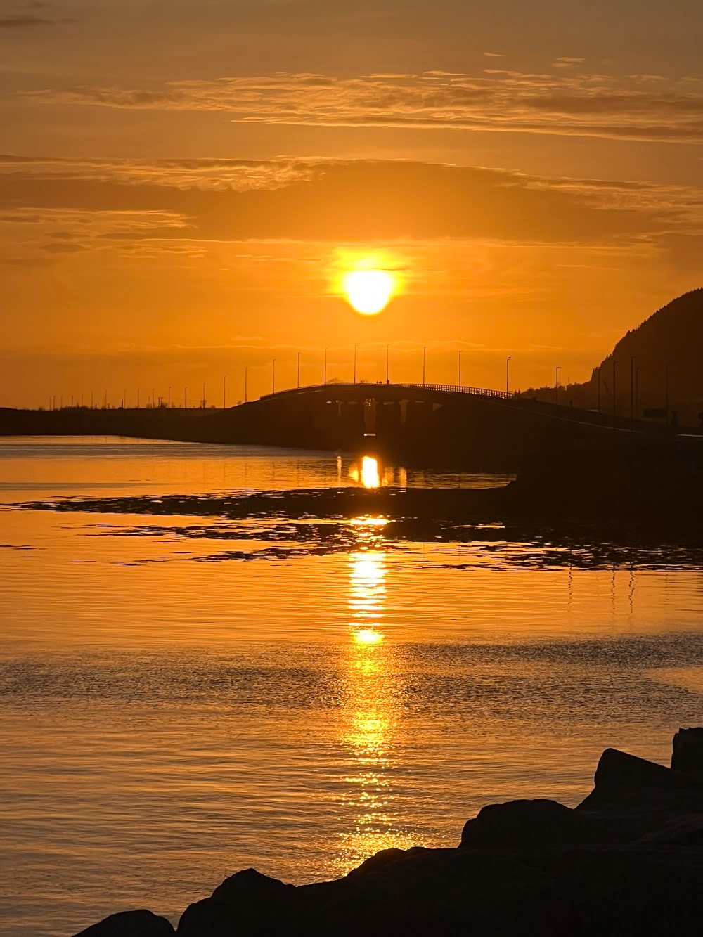 A bright orange sunset over calm fjord waters in S&oslash;vik